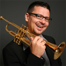 Dieses Bild zeigt den Leiter der HSD Big Band Martin Reuthner. Ein Mann mit dunklen Haaren und Brille. Er hält eine Trompete in der Hand.
